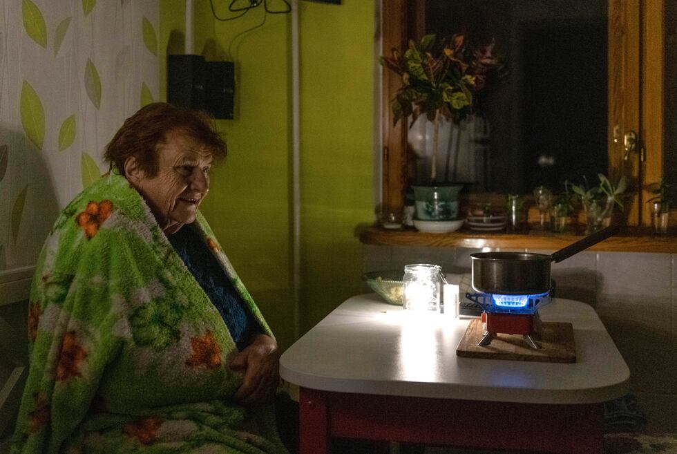 An elderly woman cooks food on a gas burner during a blackout in Kyiv, Ukraine, Monday, Nov....